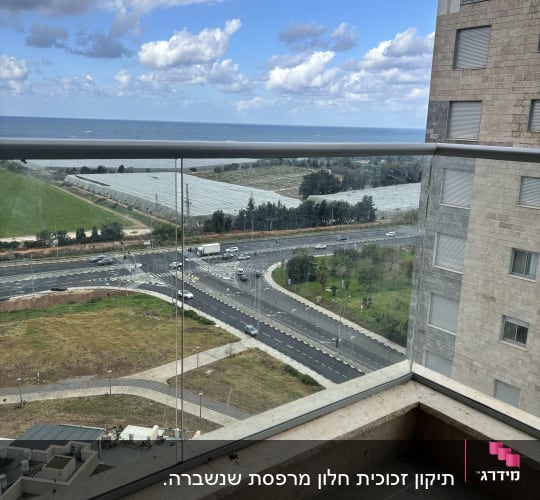 מעקה זכוכית במרפסת עם נוף לים ולבניין סמוך